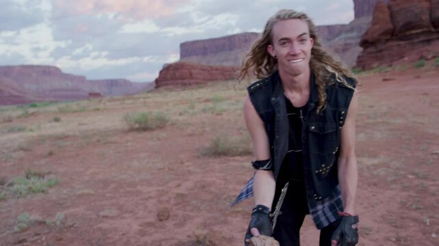 Funny man picking up cow pie and throwing it in desert - dusk