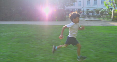 Young boy running joyfully through a grassy park, wearing a white shirt, with a happy expression, surrounded by greenery, enjoying an energetic and playful moment outdoors