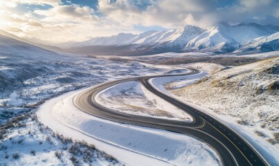 Aerial drone view of highway winding through snowcapped landscape with mountains