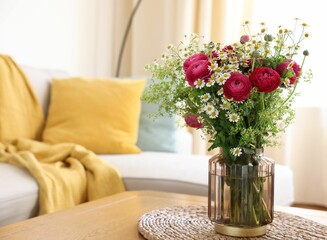 Beautiful ranunculus flowers and chamomiles in vase on table indoors
