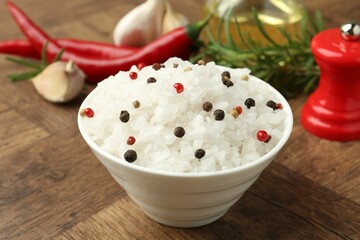 Sea salt and spices in bowl on wooden table, closeup