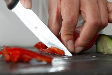 Close-up of a woman's hands cutting vegetables with a knife on a cutting board. Home cooking concept, gastronomy, veganism.