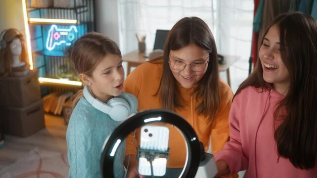 Teenage girls' friends singing karaoke recording video content for social networks, having fun at home dancing using selfie camera on the smart phone