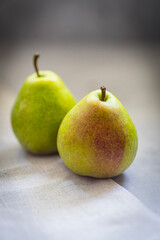 Ripe pears with reddish spots on a light surface. A few fruits are blurred in the background.