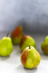 Ripe pears with reddish spots on a light surface. A few fruits are blurred in the background.