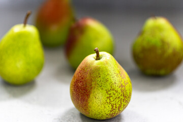 Ripe pears with reddish spots on a light surface. A few fruits are blurred in the background.
