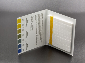 Urine pH diagnostic strips with scale closeup on black.