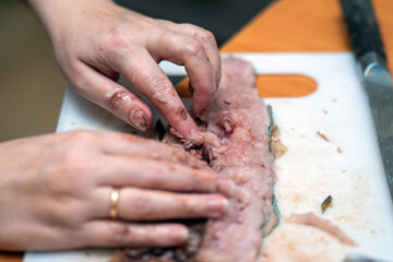 Delicate hands skillfully navigate through fish, meticulously removing bones to prepare a fresh fillet, highlighting the artistry and care in culinary preparation