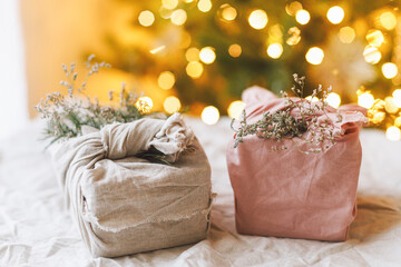 Stylish zero waste gifts on rustic table on background of christmas tree with lights. Merry...