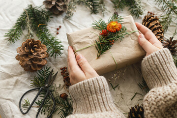 Hands holding stylish christmas gifts with fir branch on rustic table with natural ornaments .Zero waste Christmas. Sustainable presents, winter holiday present