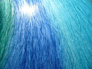 Delicate, airy, blue and turquoise material wrinkled in wind and sunlight - abstract background. Topics: texture, pattern, weather, wind, atmosphere, season, sunny season, vacation, relaxation, rest