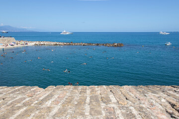 Looking over the ancient walls of Antibes in the south of France to the beach, yachts and people swimming in the sea