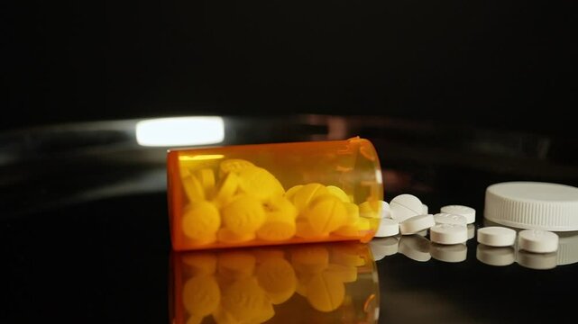 Prescription pills fall on the table from the bottle in slow motion. Pharmaceutical opioid painkillers crisis in America. Narcotic abuse adn addiction overdoses.  Macro close up shot.