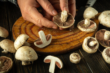 Male hands holding champignon or agaricus mushroom. Sorting and cleaning mushrooms on the kitchen...