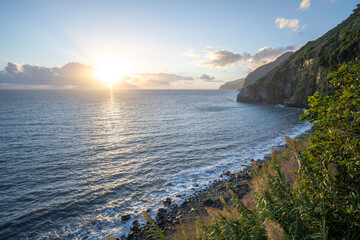 Sunlight shines through the clouds over the sea on a rocky coastline in the morning. Seixal beach, Madeira Island, Portugal, Europe.