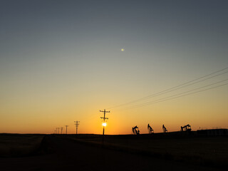 The sun rises behind transmission lines and pumpjacks in North Dakota