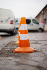 Traffic cone in the parking lot. Orange color with a white stripe