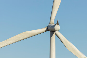 Close-up of large wind turbine nacelle hub and blades against clear blue sky at renewable energy...