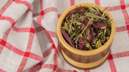 Wooden container filled with dried herbs for Ecuadorian horchata tea, placed on a checkered cloth. Great for rustic, homemade health products, herbal remedies, and traditional drink promotions