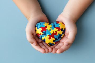 Little child hand holding colorful heart on light blue background. World autism awareness day concept