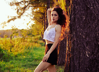 Beautiful happy slim health body woman posing in fashion clothing near the huge tree on sunset...
