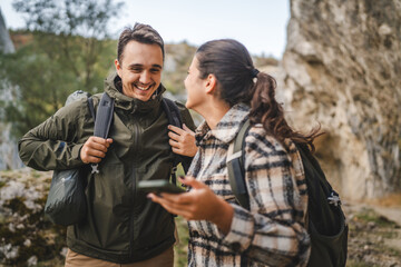 Fototapeta premium couple take a break from hiking and use mobile phone having fun