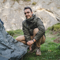 Adult man camper sett up a camping tent in outdoor green setting