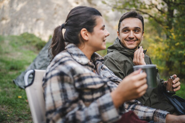 Boyfriend and girlfriend campers sit in front tent, enjoy the drink