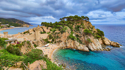 Fototapeta premium Beautiful panoramic view of Tossa de Mar fortification, rocky cliffs, trees and Es Codolar beach. Turquoise water of the Mediterranean Sea. Costa Brava, Catalonia, Spain