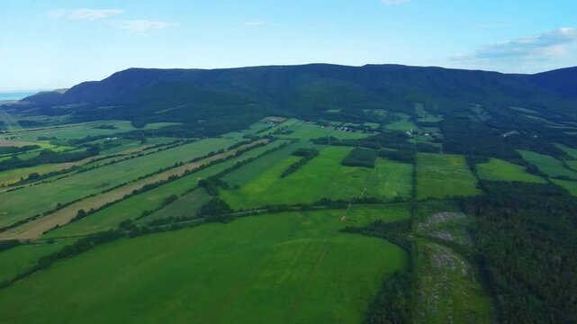 Aerial Panoramic View of Lush Green Appalachian Mountains and Cultivated Fields Bordering the Sea Under Clear Sky in Carleton‑sur‑Mer, Quebec