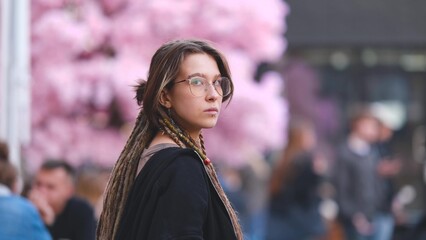 Fototapeta premium Portrait of a beautiful young woman with dreadlocks on a city street. A girl is sitting on the street in the food court area with a glass of coffee in her hand. She is getting ready to meet her