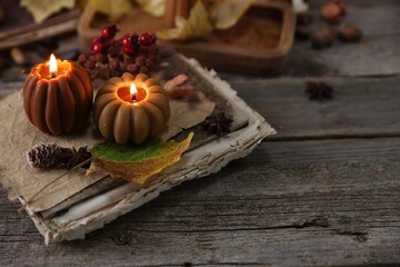 Fototapeta premium Burning candles in shape of pumpkins, old book and autumn decor on wooden table, closeup