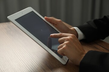 Businesswoman using tablet at wooden table indoors, closeup. Modern technology