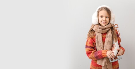 Cute little girl holding ice skates against light background with space for text