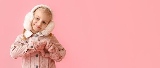 Little girl in stylish winter clothes showing heart shape with her hands on color background