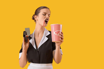 Young woman dressed for Halloween as maid with popcorn and knife on yellow background