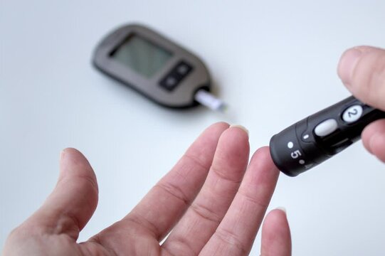 Caucasian person pricking their finger with a small lancet for a blood glucose level screening. Diabetes Mellitus test. Sliding video.