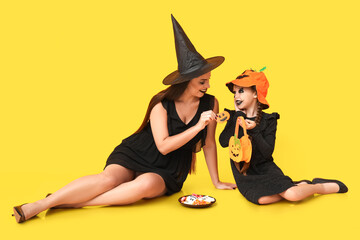 Little girl and her mother dressed for Halloween with treats on yellow background