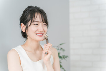 美顔器でマッサージするルームウェア姿の若いアジア人女性
