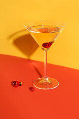 Glass of cocktail with Christmas balls on color background
