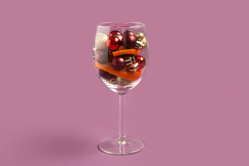 Glass with beautiful Christmas balls and orange slices on color background