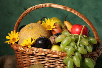 Wicker basket with different fresh fruits on green background