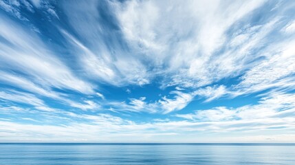 Obraz premium A wide-angle shot of a blue sky with white, wispy clouds over a calm blue ocean horizon.
