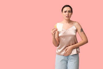 Beautiful young woman with tampon and menstrual pad suffering from menstrual cramps on pink...
