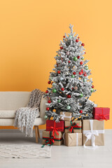 Decorated Christmas tree with gifts and sofa against orange wall