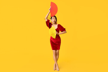 Beautiful young happy Asian woman with fans on yellow background. Chinese New Year celebration