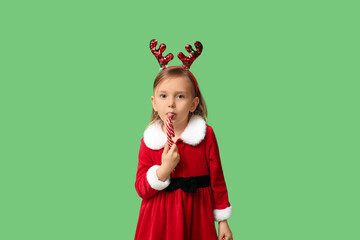 Cute little girl in Santa Claus costume with candy cane on green background