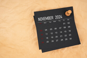 Black calendar sheet for November 2024 with thumbtack on brown paper crumpled.