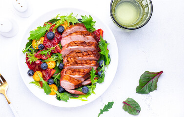 Foodie food salad with baked duck fillet, bloody oranges, kumquat, blueberries and mixed greens, white background, top view