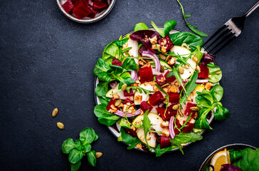 Yummy vegan salad with beet, pear, nuts, pumpkin seeds and lettuce, black background, top view